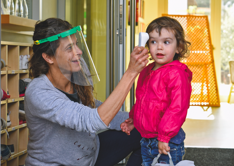 Una professora pren la temperatura a una alumna en una escola bressol. 
