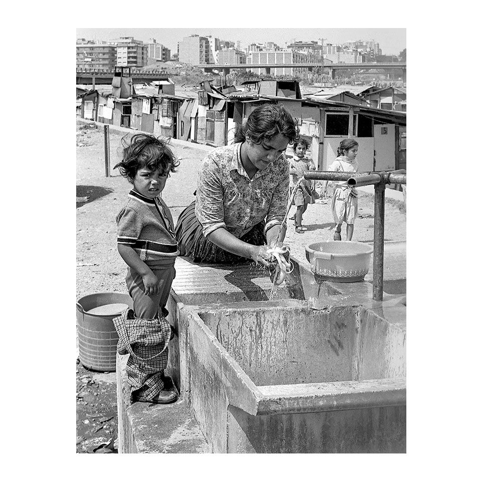 L’aigua, un luxe col·lectiu  Una dona renta roba a l’única font del campament mentre la seva filla observa. Un gest domèstic que esdevé símbol de resistència enmig de l’adversitat. Any: 1982 – Fotografia de Vicenç Semper