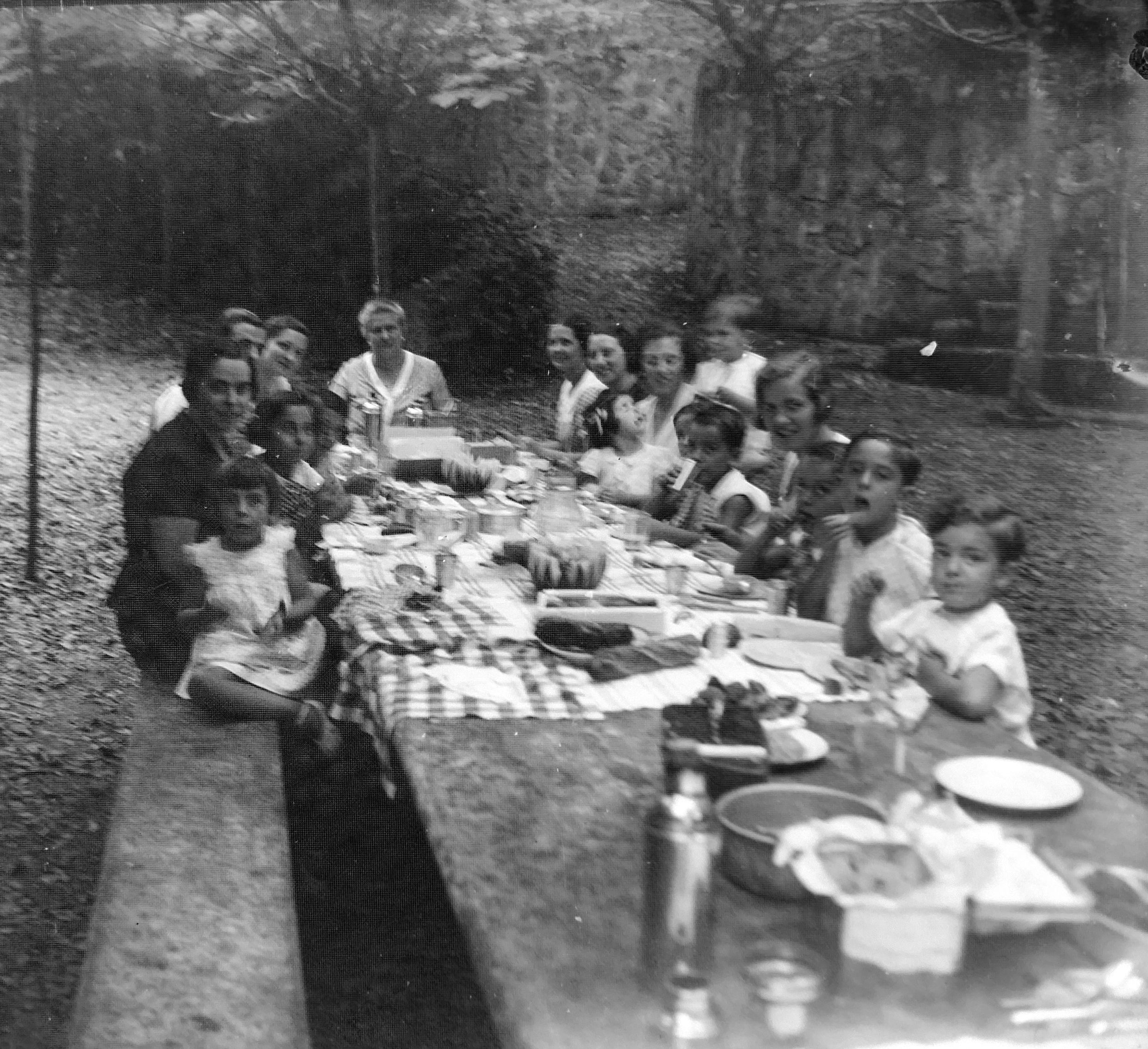 Taula d’estiu. Gran àpat familiar a l’ombra d’un jardí. Dones i criatures comparteixen taula i estiu. Una escena domèstica que ens apropa al dia a dia d’unes vacances llargues. Família Recolons / @GREC