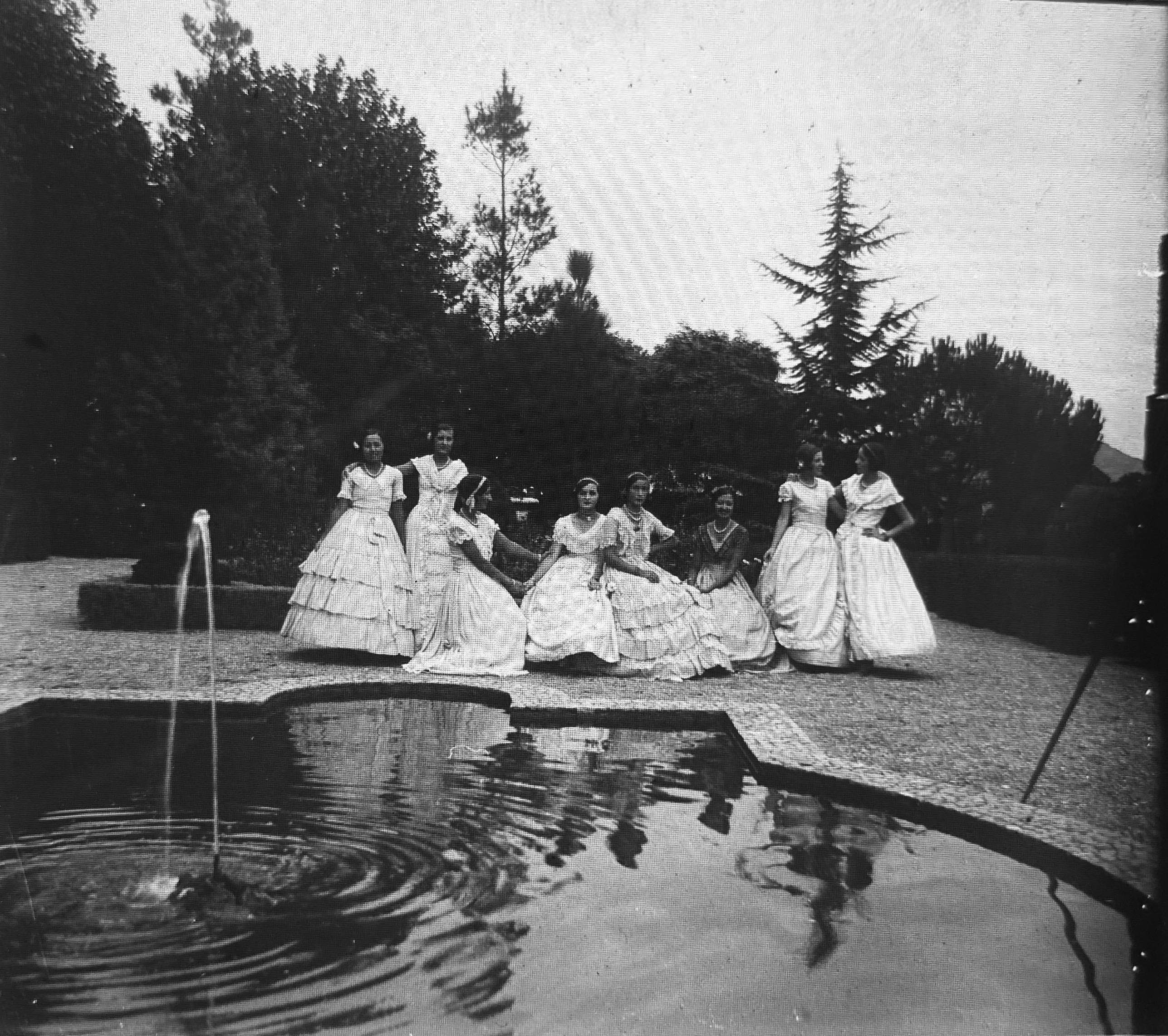 Dames de blanc als jardins. Un grup de noies joves, vestides amb elegància, posen davant d’una font decorativa. L'escena evoca les trobades socials de l’estiueig burgès. FOTO: Família Recolons / @GREC Dames de blanc als jardins. Un grup de noies joves, vestides amb elegància, posen davant d’una font decorativa. L'escena evoca les trobades socials de l’estiueig burgès. FOTO: Família Recolons / @GREC