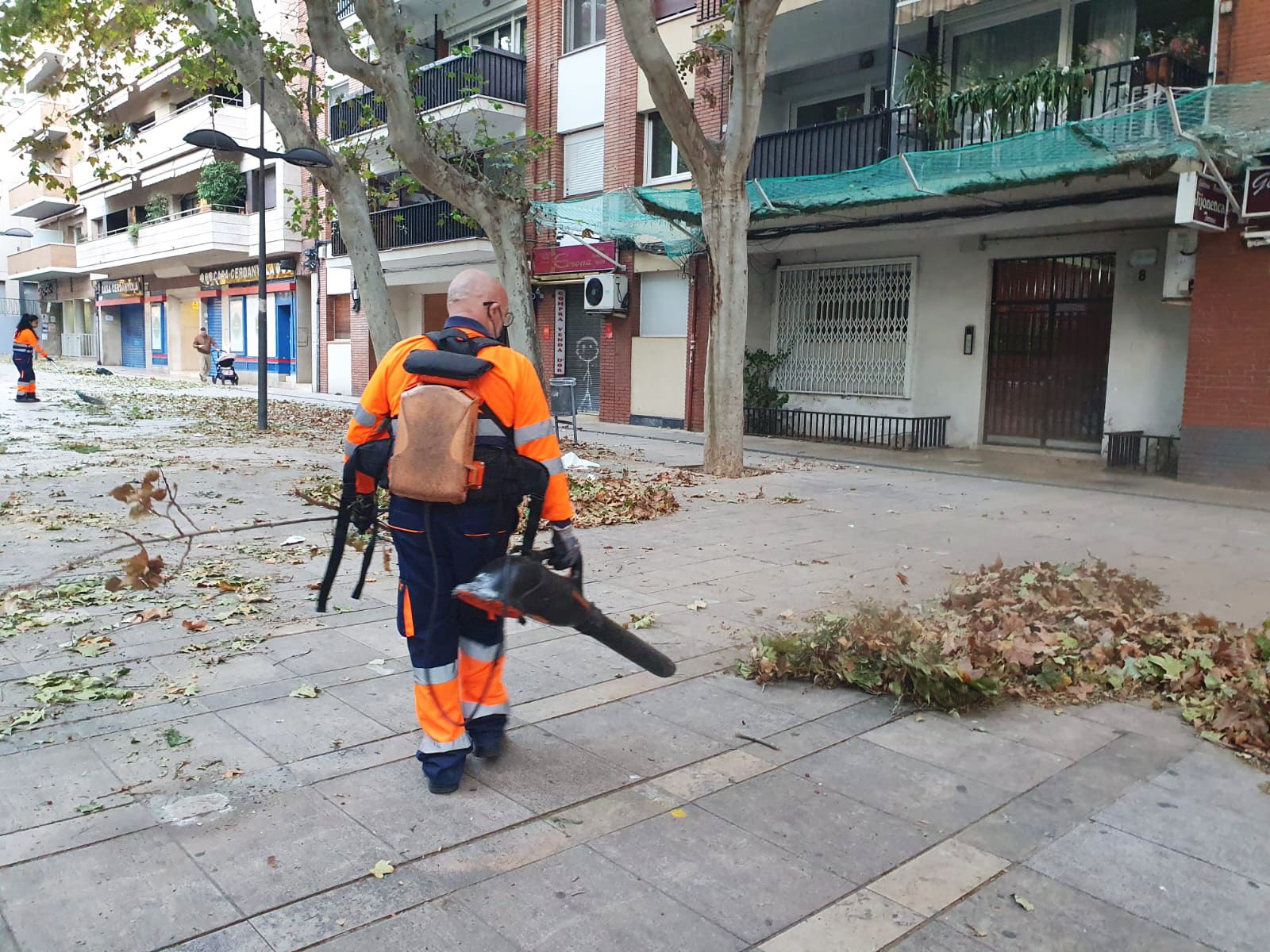 Dos operaris de la brigada escombren i bufen les fulles que cobrien la plaça Enric Granados. Foto: Judit Josa. Dos operaris de la brigada escombren i bufen les fulles que cobrien la plaça Enric Granados. Foto: Judit Josa.