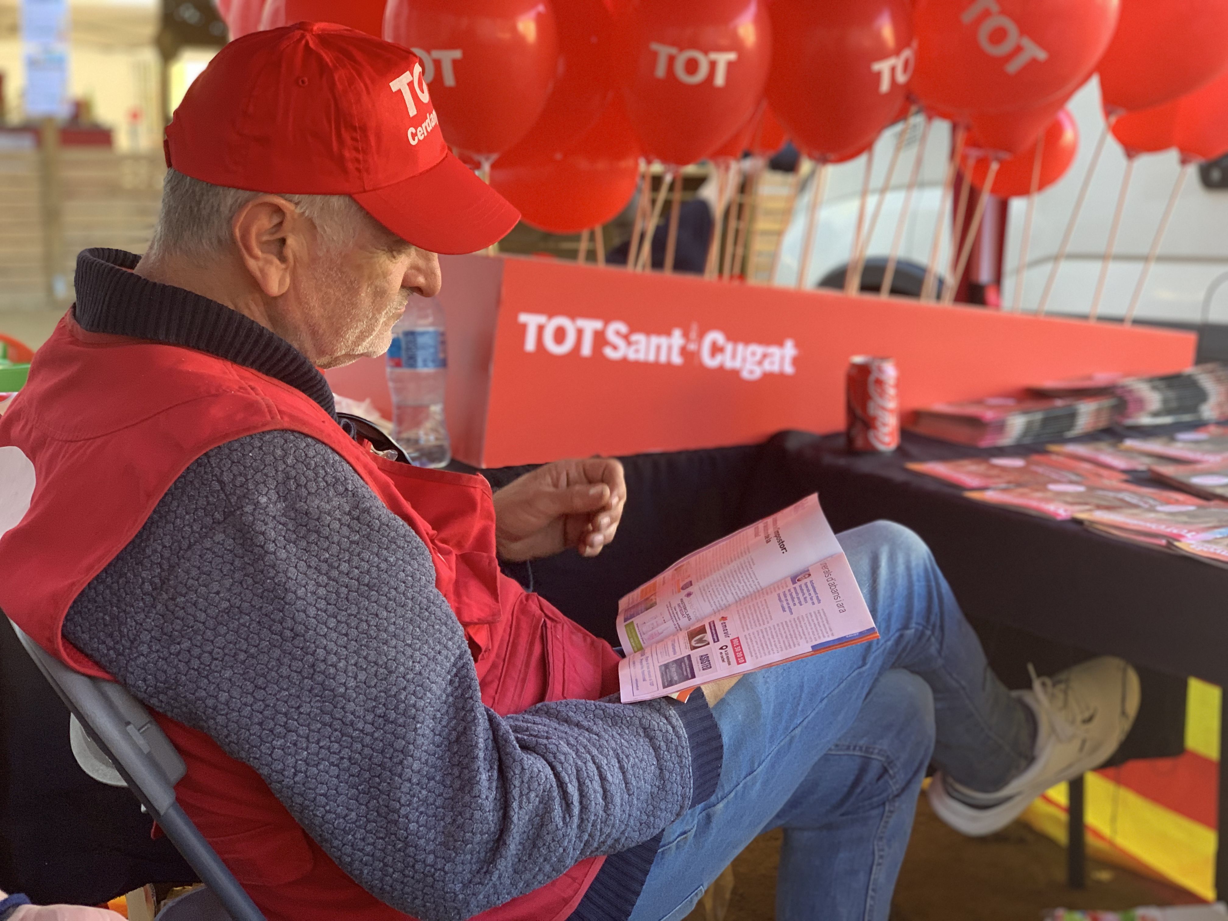 Un membre del TOT Cerdanyola llegint el setmanari durant la Festa de Tardor. Al fons, la parada amb material reutilitzat del TOT Sant Cugat, en clau sostenible.