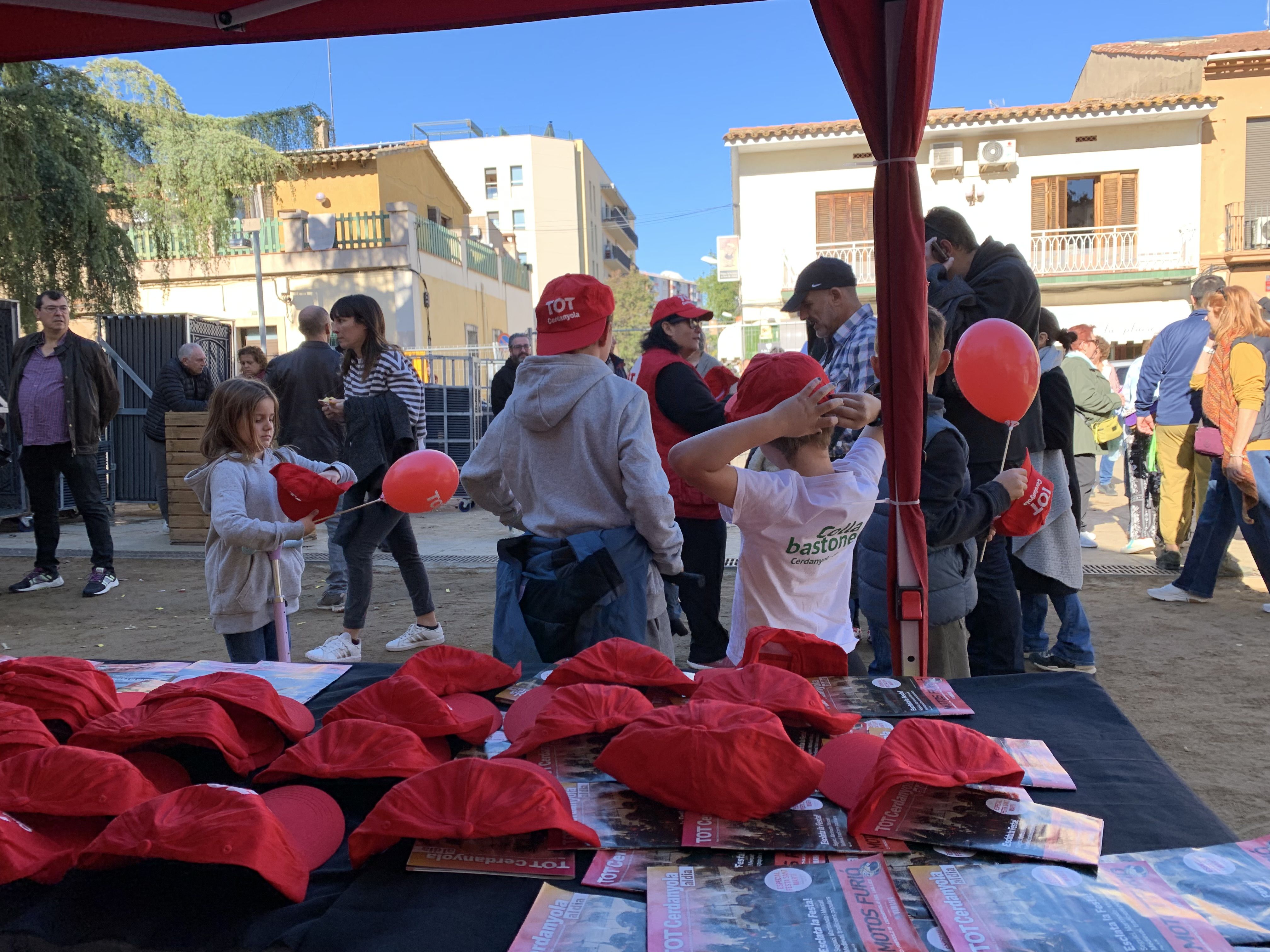 Veïns i veïnes s’acosten a la parada del TOT Cerdanyola durant la Festa de Tardor per endur-se revistes, globus i gorres.