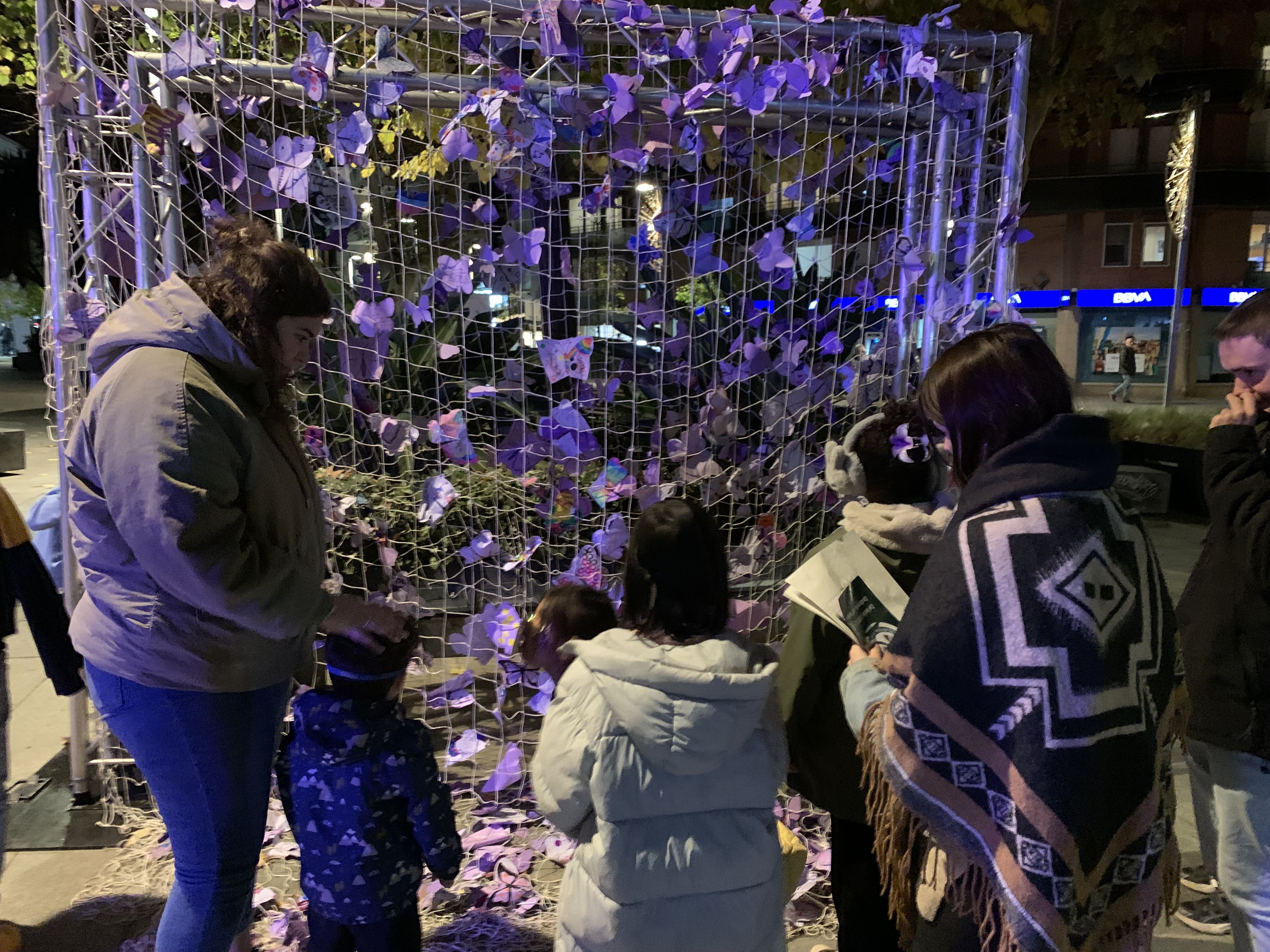 Una família contempla les papallones lila, símbol de denúncia local, penjades en una xarxa a la plaça de l'Abat Oliba el 25 N. FOTO: Judit Josa