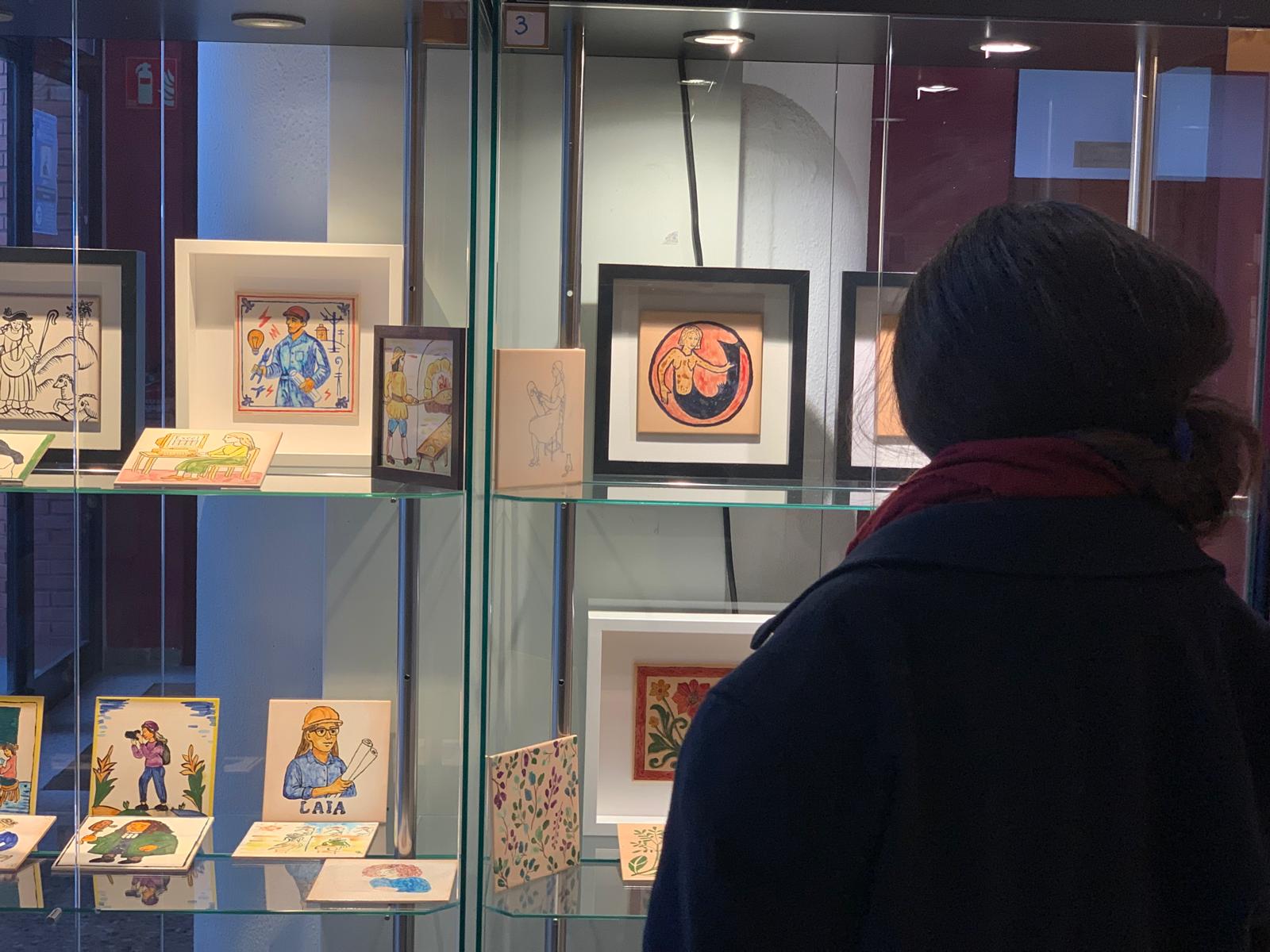 Una dona mira les rajoles d'arts i oficis que han creat els alumnes del taller de ceràmica de l'escola de les Arts de l'Ateneu, exposades al vestíbul. FOTO: Judit Josa.