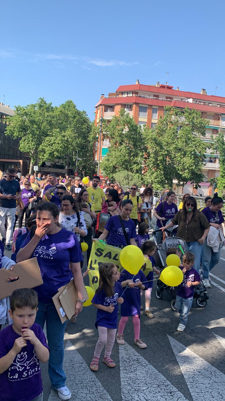 Famílies, infants i docents de La Sínia durant la tercera mobilització al carrer de Francesc Layret abans del ple municipal, amb globus grocs i samarretes liles en defensa de l’escola pública.