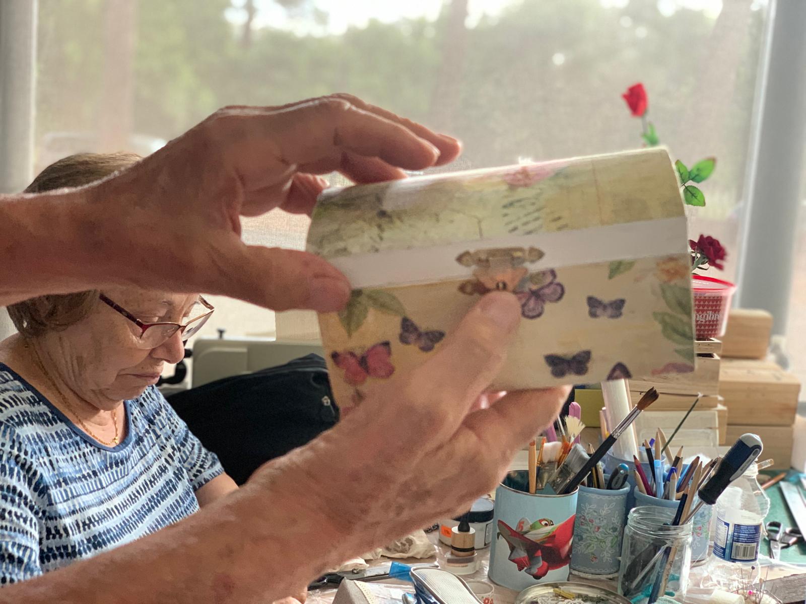 Un voluntari mostra una capsa decorativa durant una de les activitats de manualitats d’Aspadi, mentre les professores preparen el taller. FOTO: Judit Josa