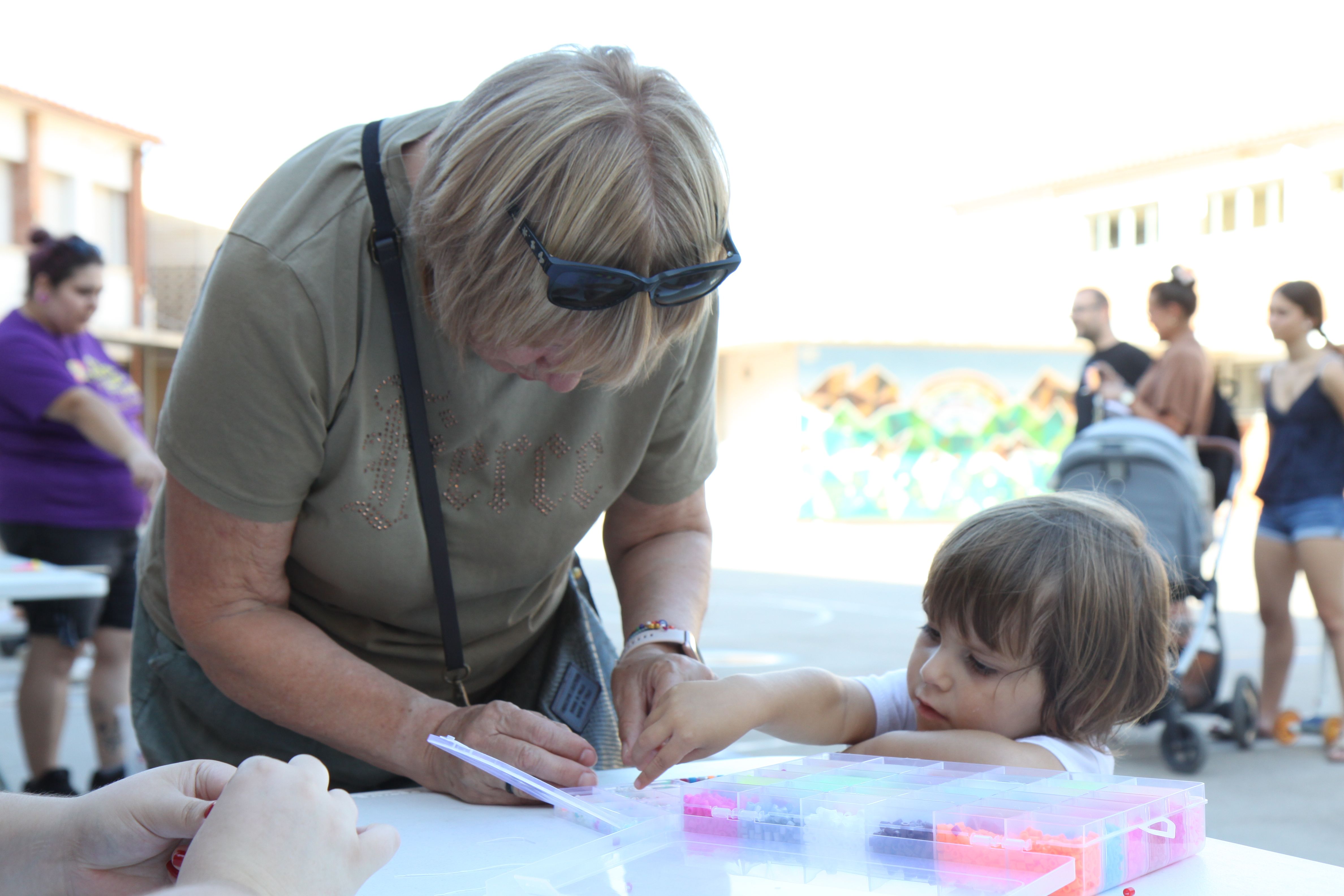 Una àvia ajudant la seva neta a fer una polsera. Foto: Laia Jubany