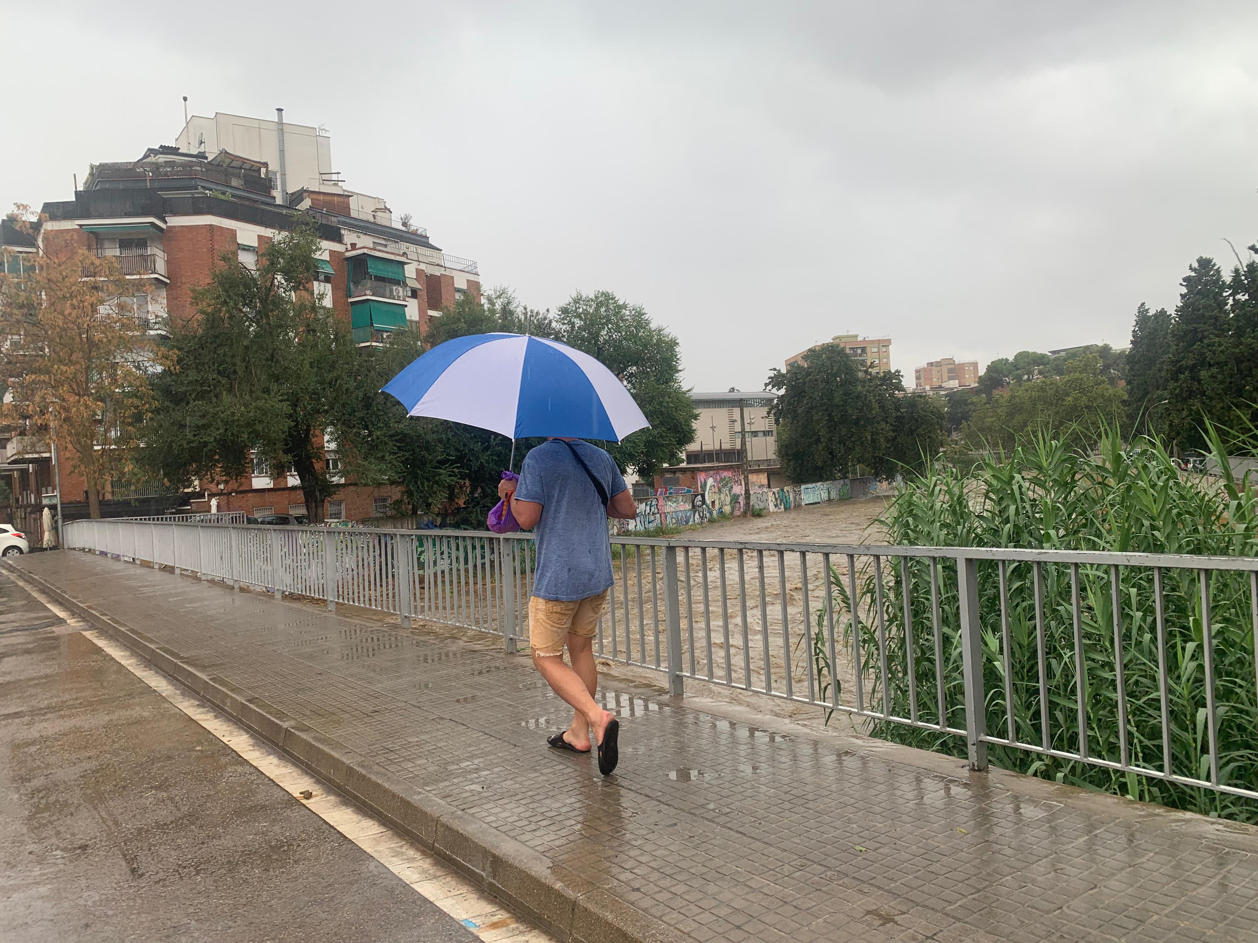 Un vianant travessa sota la pluja de migdia el pont sobre el riu Sec. FOTO: Judit Josa